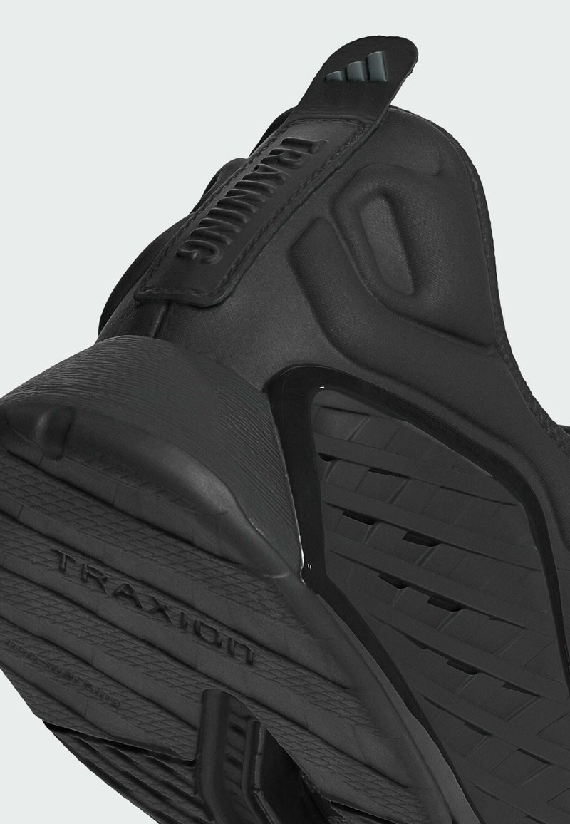 Scarpa da ginnastica nera con suola in gomma testurizzata, presenta un motivo a tassello triangolare e un tallone rinforzato. È visibile il marchio "TRAXION".