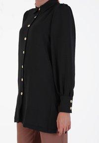 Black button-up shirt with long, puffed sleeves and gold buttons. Smooth, lightweight fabric; straight hem and cuff detailing.