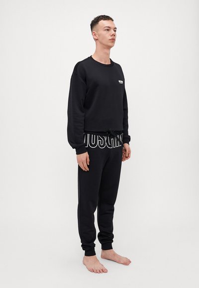 Black sweatshirt with a crew neck and white logo on the left chest, paired with matching sweatpants featuring a bold printed waistband.