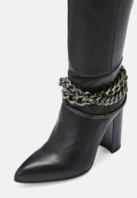 Mustat nahkasaappaat nilkkapituisina, joissa on terävä kärki, loiva korko ja hopeiset ketju yksityiskohdat nilkan ympärillä lisäämään tyyliä.