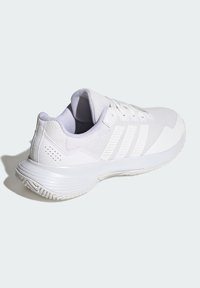 Biały but sportowy z fakturowaną cholewką z siateczki, żebrowanymi detalami i gładką gumową podeszwą. Posiada cienkie sznurowadła oraz trzy równoległe paski.