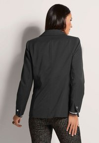 Schwarzer maßgeschneiderter Blazer mit Reverskragen und langen Ärmeln, der mit silberfarbenen Knopfakzenten und einer schlanken Form versehen ist.