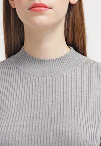 Pull en maille côtelée gris avec un col montant, présentant une texture fine et un motif uniforme, mettant en valeur un gros plan des détails du tissu.