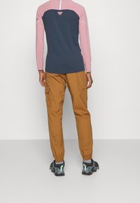 Long-sleeved top with a navy body and pink sleeves, paired with brown cargo pants. Features include a logo on the back and elastic cuffs.