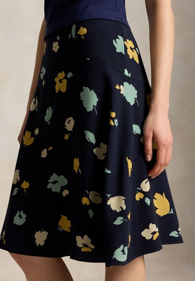 Jupe trapèze bleu marine avec des motifs floraux jaunes, verts clairs et beiges, portée avec un top bleu foncé, vue de profil de la taille aux genoux.