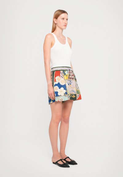 White tank top paired with a multicolored floral patterned mini skirt featuring an elastic waistband. Black slip-on shoes complete the outfit.