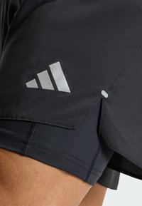 Pantalones cortos deportivos negros con un logo plateado contrastante y una abertura lateral. Presentan una textura suave y costuras planas para mayor comodidad.