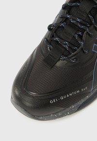Pantof sport negru cu vârf texturat, șireturi cu accente albastre și textul „GEL-QUANTUM 360” pe talpă în lateral.