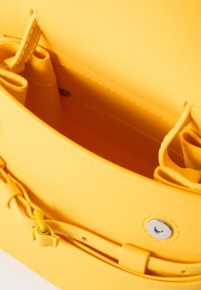 Intérieur de sac à main jaune montrant des bords cousus, une fermeture magnétique pression et des compartiments intérieurs pour l'organisation.