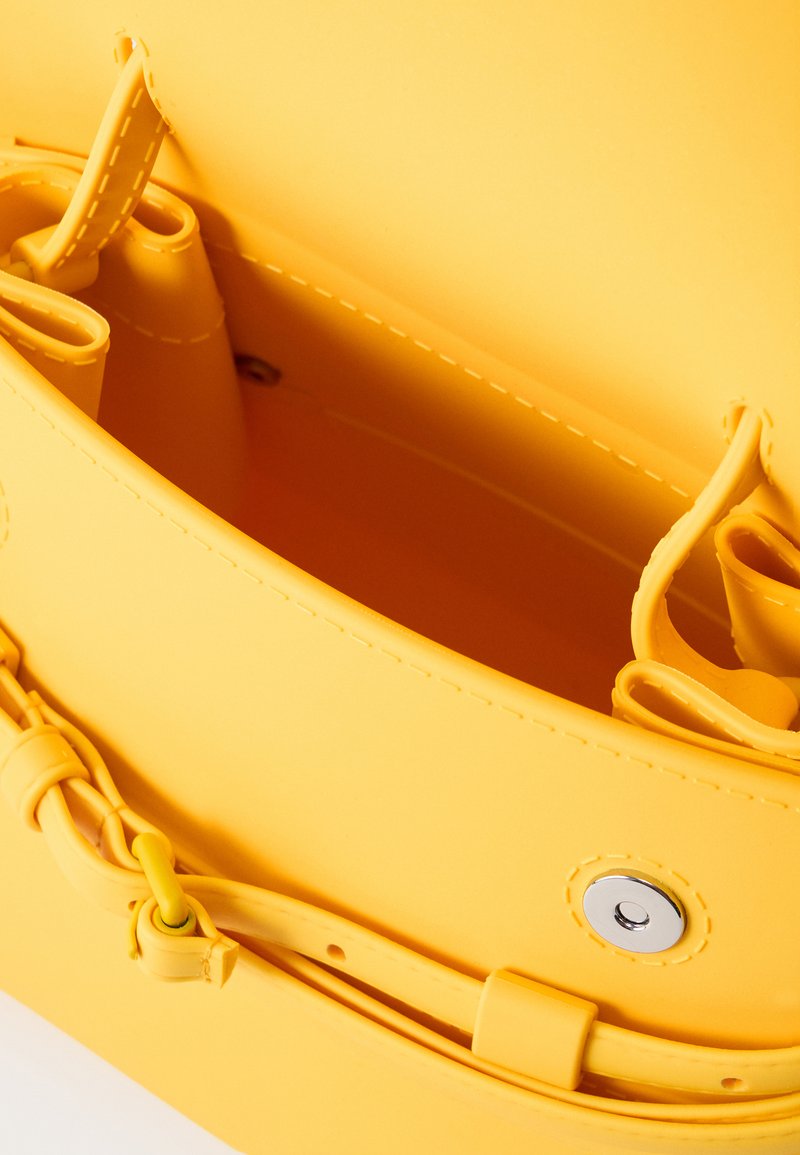 Intérieur de sac à main jaune montrant des bords cousus, une fermeture magnétique pression et des compartiments intérieurs pour l'organisation.