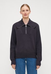 Mørk strikket genser med bred, flat krage, halvdels glidelås, ribbestrikkede ermer og hemming. Har et strukturert panel på brystet.