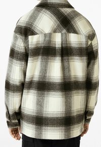 Grå och krämfärgad rutvävd flanellskjorta med knäppbar krage, långa ärmar och en något böjd nederkant. Tyget verkar mjukt och texturerat.