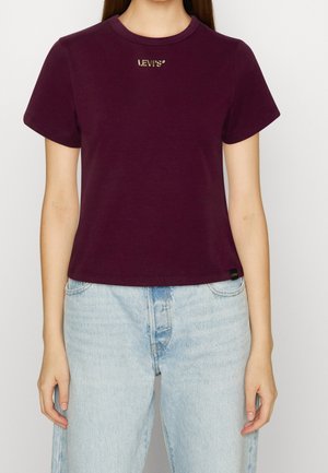 Personne portant un t-shirt Levi's violet foncé uni et un jean taille haute bleu clair, debout devant un fond neutre.