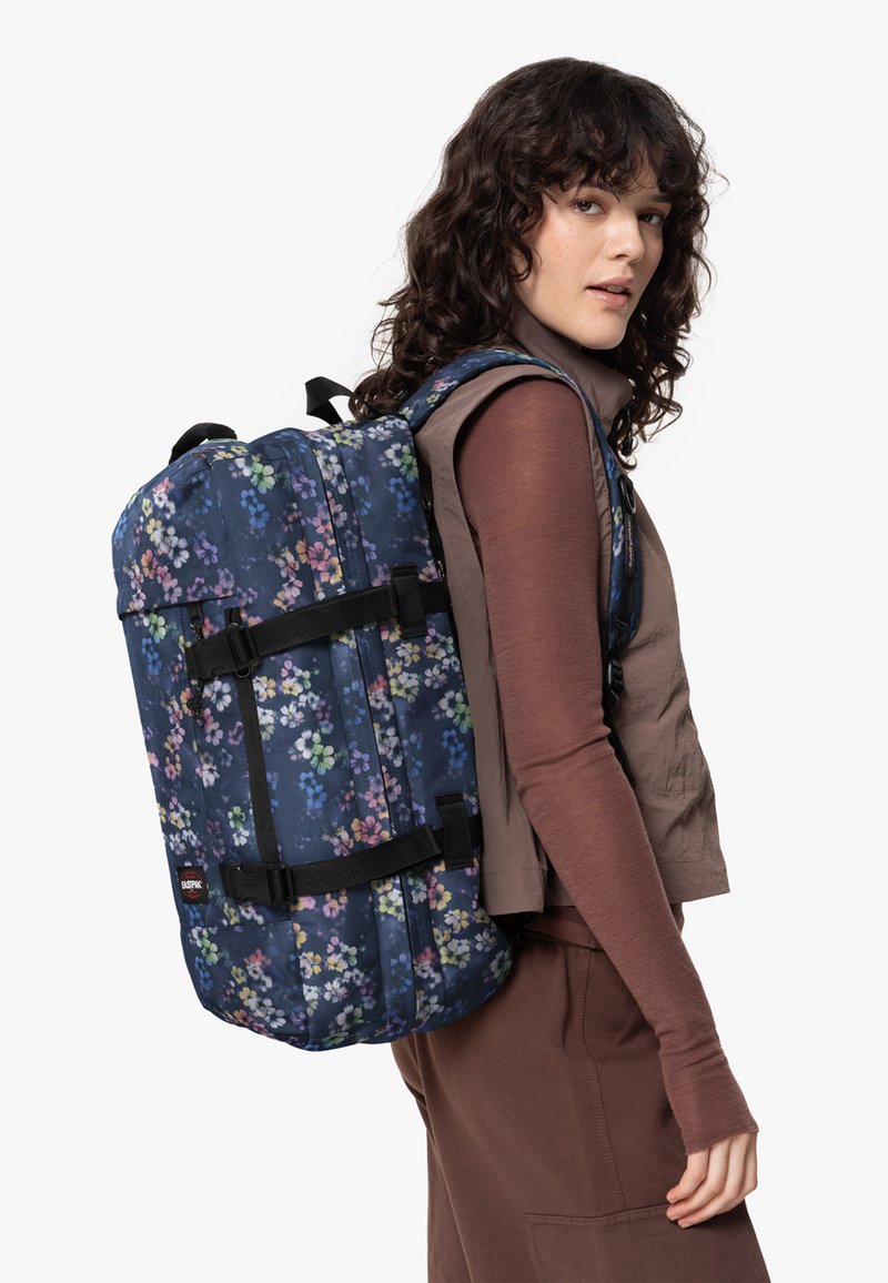 Blue floral print backpack with black straps and buckles, rectangular shape, textured fabric, and a top flap for closure.