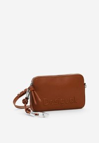 Braune Leder-Clutch mit geprägt "Desigual" Logo, Reißverschluss und abnehmbarem Handgelenkriemen. Verfügt über zwei dekorative Lederquasten.