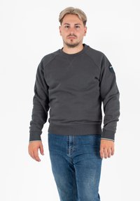 Ciemnoszara bluza z okrągłym dekoltem, ze ściągaczami na mankietach i dole. Posiada naszywkę z logo na lewym ramieniu oraz gładką fakturę.