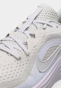 Κοντινό πλάνο λευκού αθλητικού παπουτσιού με επάνω μέρος από δίχτυ, υφασμάτινες επιστρώσεις, κορδόνια και ανεβασμένο λογότυπο Nike στη πλευρά.