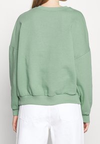 Sudadera verde de gran tamaño con dobladillo y puños acanalados. Textura suave, cuello redondo y costuras de hombro caídas.
