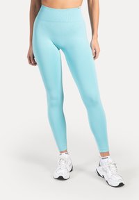 Leggings azul claro de tela elástica con una cintura alta. Textura suave y diseño ajustado, combinados con zapatillas deportivas blancas.