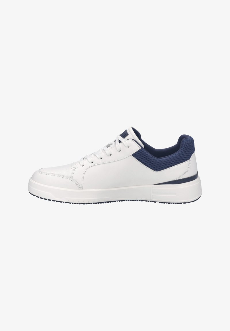 Baskets blanches basses avec un col rembourré bleu marine, des lacets blancs et une épaisse semelle blanche, vues de côté extérieur sur un fond blanc.