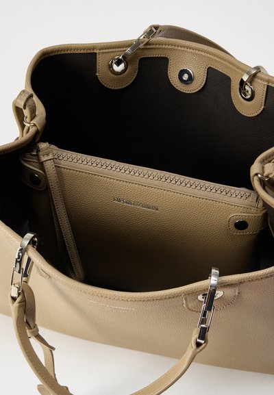 Μπεζ δερμάτινη τσάντα ώμου με ανοιχτό πάνω μέρος, ασημένια μεταλλικά στοιχεία και μαύρο εσωτερικό επένδυση. Διαθέτει φερμουάρ σε διαμέρισμα και λογότυπο με ανάγλυφη χάραξη.