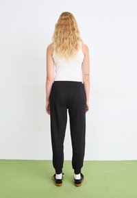Zwarte, taps toelopende sweatpants met geribbelde boorden; gedragen met een witte tanktop en zwarte schoenen. Glad materiaal; casual, ontspannen pasvorm.