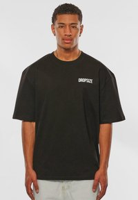 Sort kortærmet t-shirt lavet af bomuld, med en hvid "DROPSIZE" logo på venstre brystområde. Løs pasform med bred udskæring.