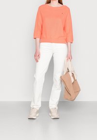 Maglione a maglia corallo con maniche a tre quarti, jeans bianchi a gamba dritta, sneakers beige chiaro e una borsa a tracolla color nocciola.