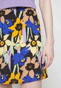 Blomster A-line nederdel i sort med store multicolor blomster i blå, gul og fersken med grønne accenter og en glat tekstur.