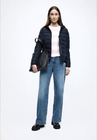 Ναυτικό μπουφάν τύπου puffer, λευκή και ροζ ανοιχτή ριγέ μπλούζα, μπλε τζιν παντελόνι με φαρδιά μπατζάκια και μαύρη τσάντα tote. Το μοντέλο φοράει μαύρες χοντρές μπότες.