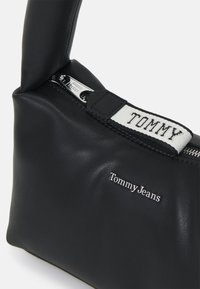 Black leather shoulder bag with a zip closure, featuring a white strap that reads "TOMMY" and silver-tone branding "Tommy Jeans."