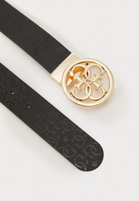 Curea neagră cu model, confecționată din material texturat, având o cataramă circulară de culoare aurie cu litere intercalate. Brandingul notabil este vizibil.