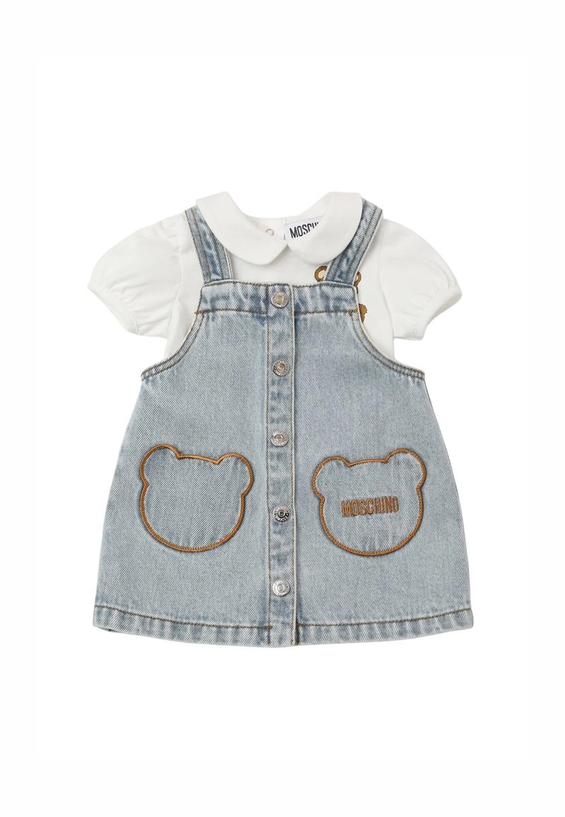 Abito da salopette in denim con un lavaggio blu chiaro, caratterizzato da tasche a forma di orso e ricamo "Moschino"; camicia bianca con maniche a sbuffo e colletto sotto.