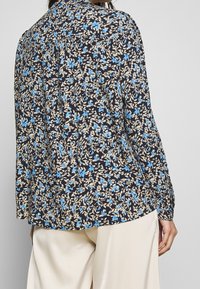 Kwiatowa bluzka w kolorze granatowym, zdobiona niebieskimi kwiatami i beżowymi liśćmi. Długie rękawy, zapinany na guziki kołnierzyk oraz luźny krój zapewniający wygodę.