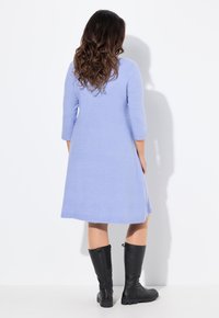 Abito a maglia azzurro chiaro con maniche a tre quarti, taglio ad A, che arriva a metà coscia, abbinato a stivali neri fino al ginocchio.