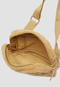 Beige Umhängetasche aus Kunstpelz mit weicher Textur, Reißverschlussverschluss und beiger Innenauskleidung. Verfügt über einen tanfarbenen Tragegurt und goldfarbene Hardware.