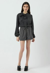 Donkergrijze, lange mouwen trui met een strikcollar, gecombineerd met grijze, geplooide shorts met elastische taille. Model draagt zwarte instappers.
