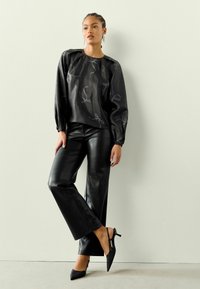 Juoda, ilgomis rankovėmis, satino bluzonė su šviesiai pilkomis kaspino raštais, derinama su juodomis aukštu liemeniu dirbtinės odos kelnėmis ir juodomis atvirais kulniukais.