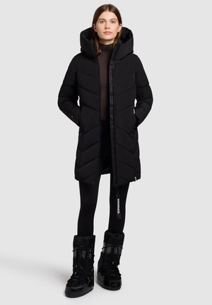 Black puffer coat with a hood, featuring a chevron pattern, zip front, and two side pockets. Worn with black leggings and insulated boots.
