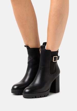 Botas negras hasta el tobillo de piel, con una suela gruesa y estriada. Cuentan con un cierre lateral, un acento de hebilla metálica y una pestaña de tela para tirar.