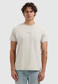Lichtgrijze katoenen t-shirt met korte mouwen, ronde halslijn en zwarte tekst "PURE PATH" gecentreerd op de borst. Soepele textuur, ontspannen pasvorm.