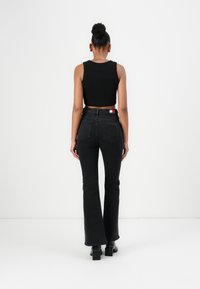 Cropped black tank top paired with black flared jeans. Notable details include a logo patch on the waistband and chunky black heeled boots.