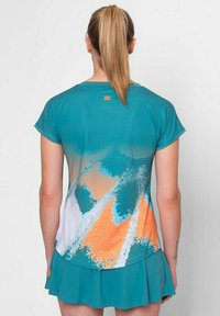 Camisa deportiva verde azulado con un diseño degradado que presenta patrones abstractos en naranja y blanco. Mangas cortas y textura suave para mayor comodidad.