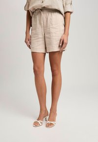 Leinenmischung-Shorts in hellbeige, mit elastischem Bund, Kordelzug und zwei Seitentaschen. Getragen mit weißen, verstellbaren Absatzsandalen.