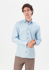 Light blue long-sleeve shirt with a standard collar, featuring dark buttons and a smooth texture, worn with beige trousers.