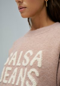 Różowy sweter o textured, pętelkowym wzorze z białym napisem "SALSA JEANS".  Żebrowany kołnierz i mankiety, wykonany z miękkiej dzianiny.