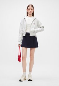 Γκρι κοντό hoodie, λευκή μπλούζα, μπλε φούστα σε φαρδιά γραμμή με λεπτομέρεια αστέρα, κόκκινη τσάντα, ανοιχτόχρωμες κάλτσες και μπεζ sneakers. Απλός και χαλαρός σχεδιασμός.