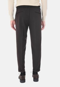 Pantaloni marrone scuro con una vestibilità affusolata, realizzati in tessuto morbido. Presentano un elastico in vita con cordoncino e due tasche posteriori.