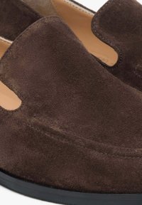 Brown suede slip-on shoes featuring cut-out side accents and a smooth inner lining. The sole is black rubber with slight texture.