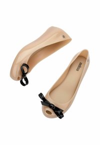 Scarpe flat color nude realizzate in materiale lucido, con un dettaglio a fiocco sulla punta e design a punta aperta. Presentano un discreto logo del brand sul lato.